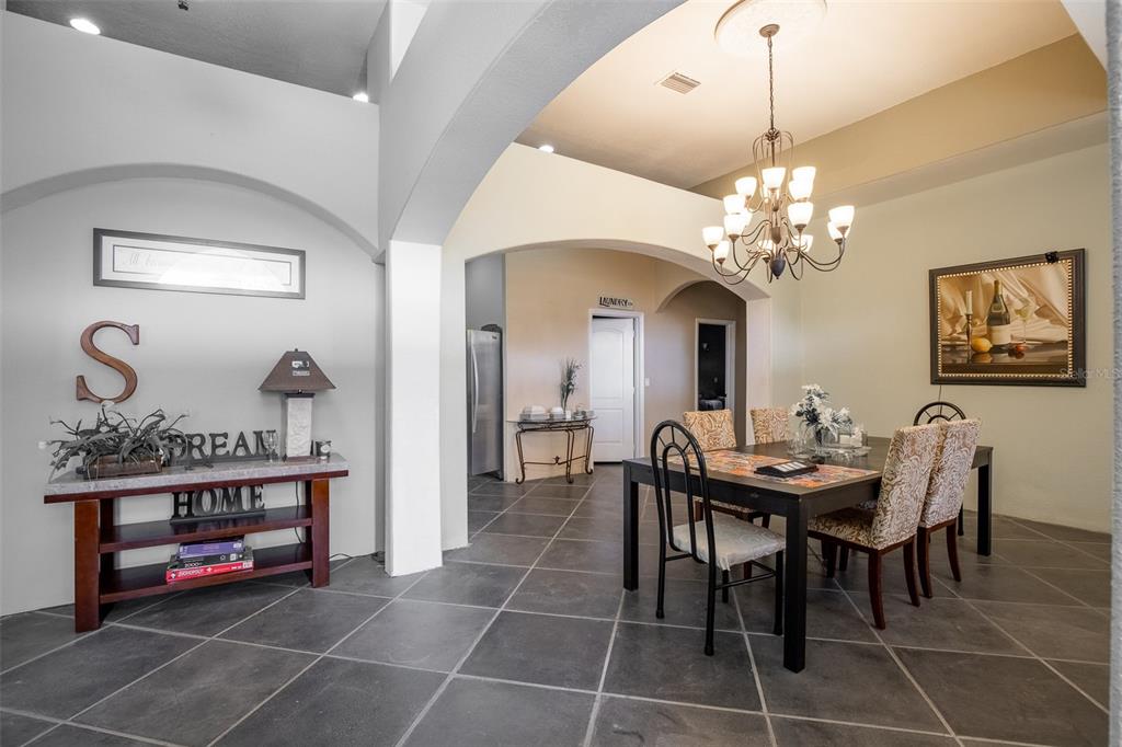 A dining room with a chandelier, dark table, and tiled floors opens to a hallway — 687 MONTURA AVENUE, CLEWISTON, FL