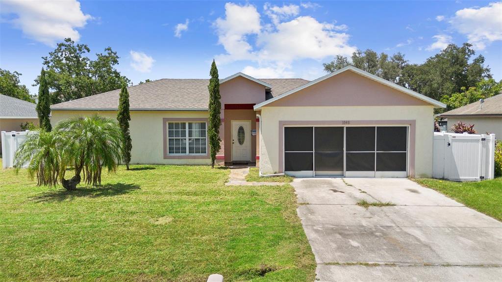 A single-story house with a beige stucco exterior, a screened garage, and a front lawn — 1040 CANNOCK DRIVE, KISSIMMEE, FL