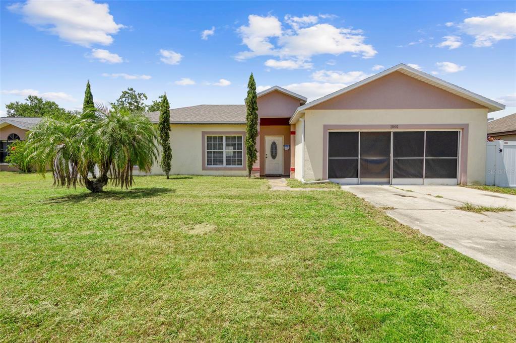 A single-story house with a beige stucco exterior, a screened garage, and a front lawn — 1040 CANNOCK DRIVE, KISSIMMEE, FL