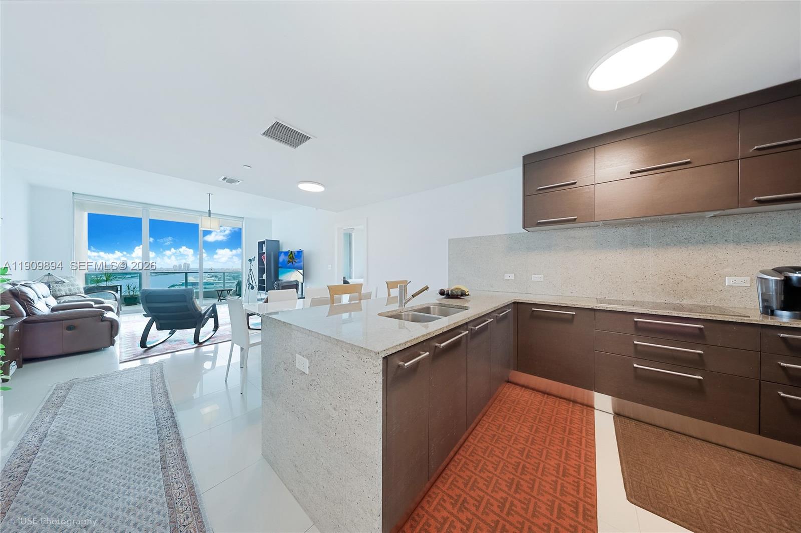 A modern kitchen with dark wood cabinets and granite countertops overlooks a living area — 900 Biscayne Blvd # 2602, Miami FL 33132, MIAMI, FL
