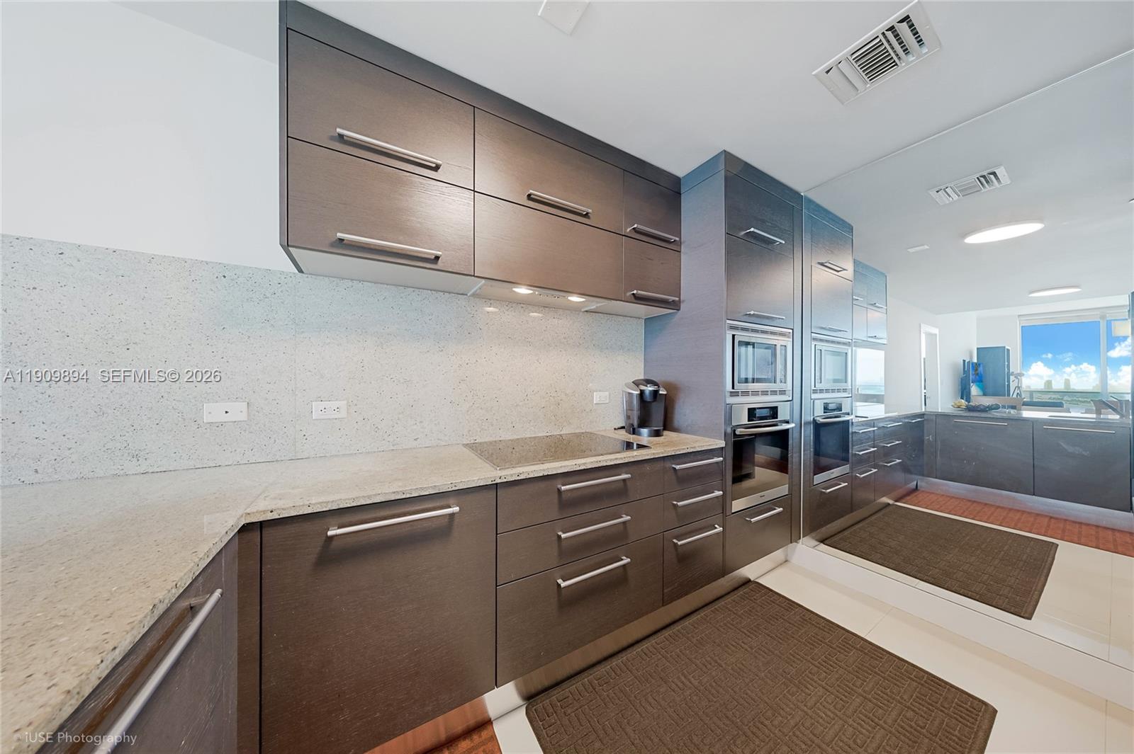 A modern kitchen features dark wood cabinetry, light speckled countertops, and built-in stainless steel appliances — 900 Biscayne Blvd # 2602, Miami FL 33132, MIAMI, FL