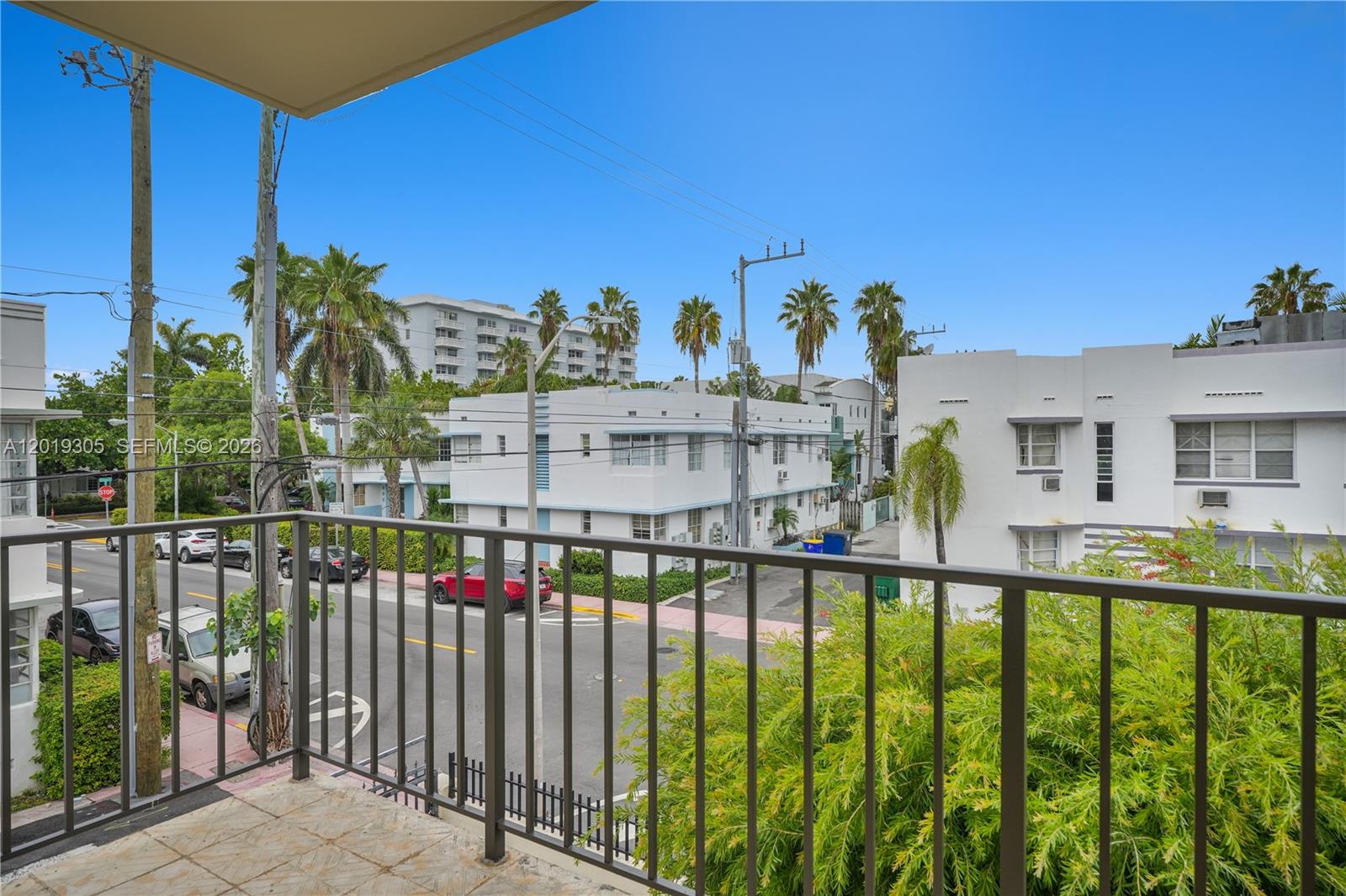 A balcony with a metal railing overlooks a street lined with white buildings and trees — 950 Euclid Ave # 201, Miami Beach FL 33139, MIAMI BEACH, FL