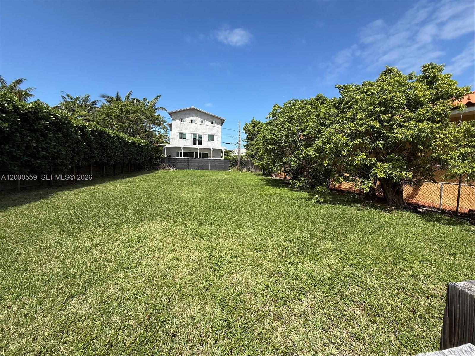 A large, grassy vacant lot is bordered by tall hedges, trees, and a neighboring house — 9308 Harding Ave, Surfside FL 33154, SURFSIDE, FL