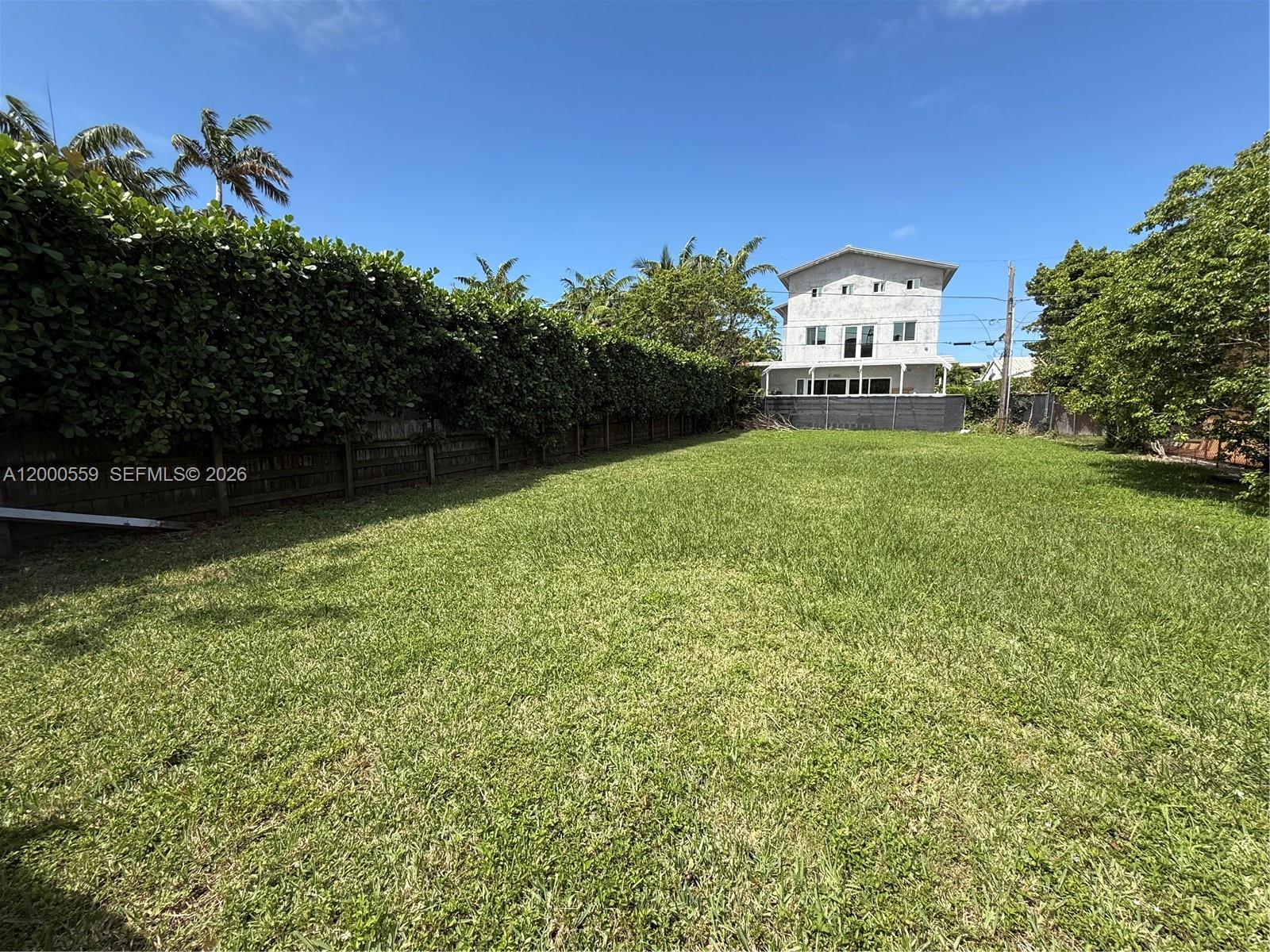 A large, grassy backyard is enclosed by a tall hedge and a wooden fence — 9308 Harding Ave, Surfside FL 33154, SURFSIDE, FL