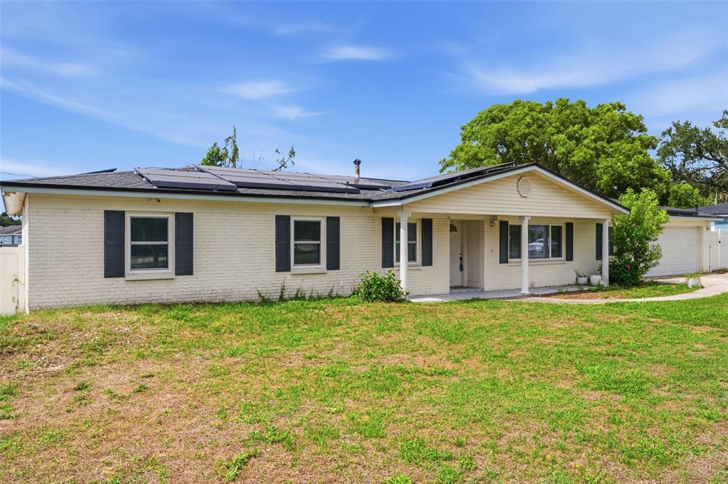 A single-story brick house with dark shutters, a covered porch, and roof-mounted solar panels — 1606 LARK LANE, BRANDON, FL