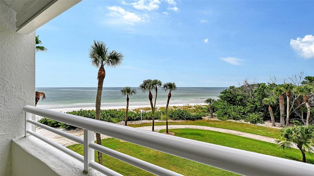 A balcony view overlooking a grassy lawn, palm trees, and the ocean under a blue sky — 240 SANDS POINT ROAD UNIT 4205, LONGBOAT KEY, FL