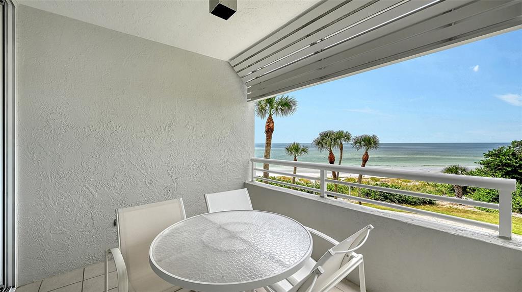 A balcony with a glass-topped table and chairs overlooks the ocean and palm trees — 240 SANDS POINT ROAD UNIT 4205, LONGBOAT KEY, FL