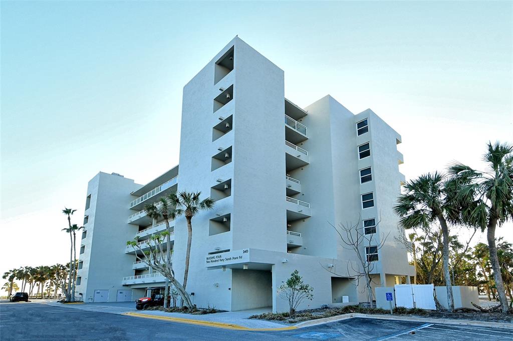A multi-story, light-colored concrete apartment building stands near palm trees and a paved parking lot — 240 SANDS POINT ROAD UNIT 4205, LONGBOAT KEY, FL