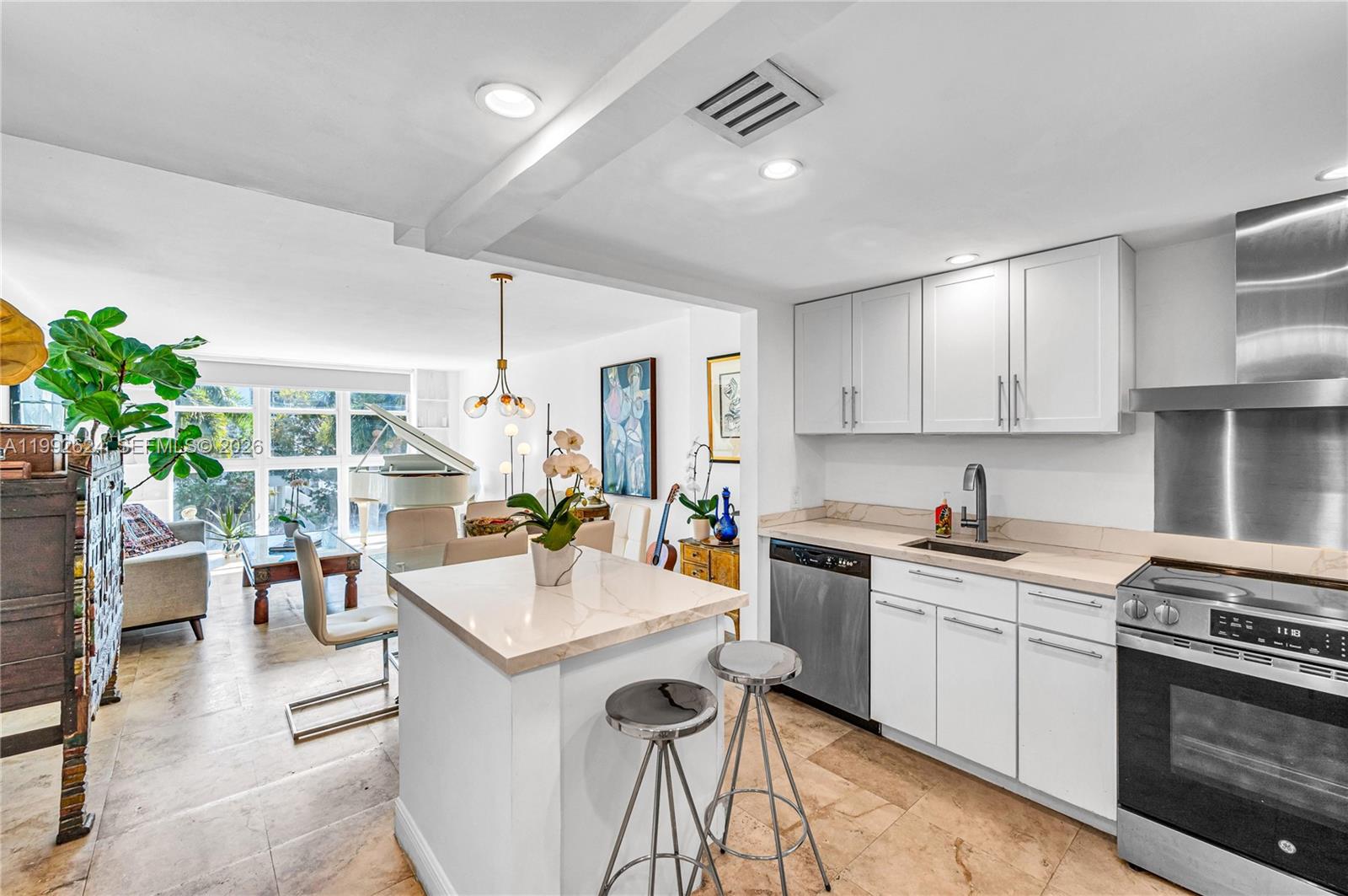 A kitchen with white cabinets and a small island opens into a bright living area — 1228 West Ave # 209, Miami Beach FL 33139, MIAMI BEACH, FL