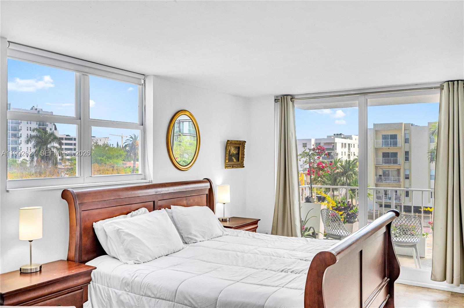 A bedroom features a wooden bed frame, white bedding, two nightstands, and large windows — 1228 West Ave # 209, Miami Beach FL 33139, MIAMI BEACH, FL