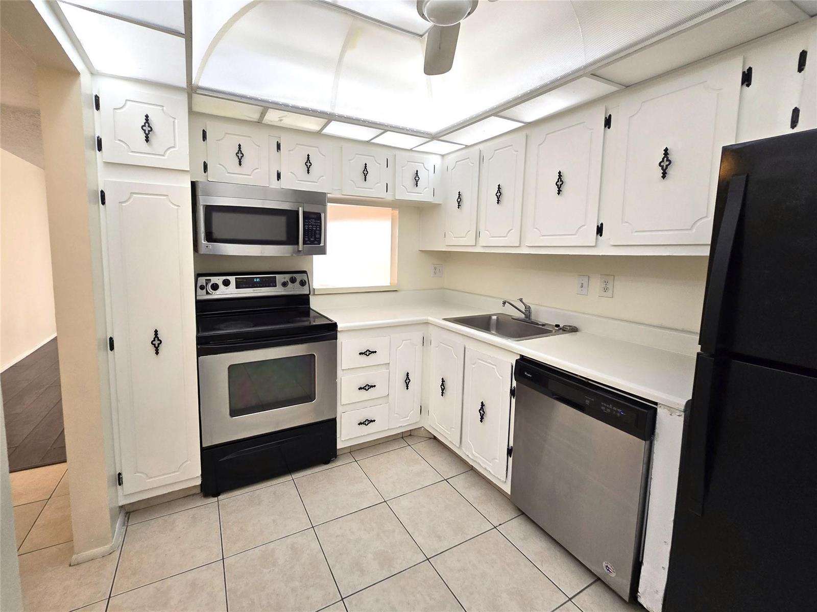 A kitchen features white cabinets with black hardware, stainless steel appliances, and tiled flooring — 4334 NW 9th Avenue # 3B, Deerfield Beach FL 33064, DEERFIELD BEACH, FL