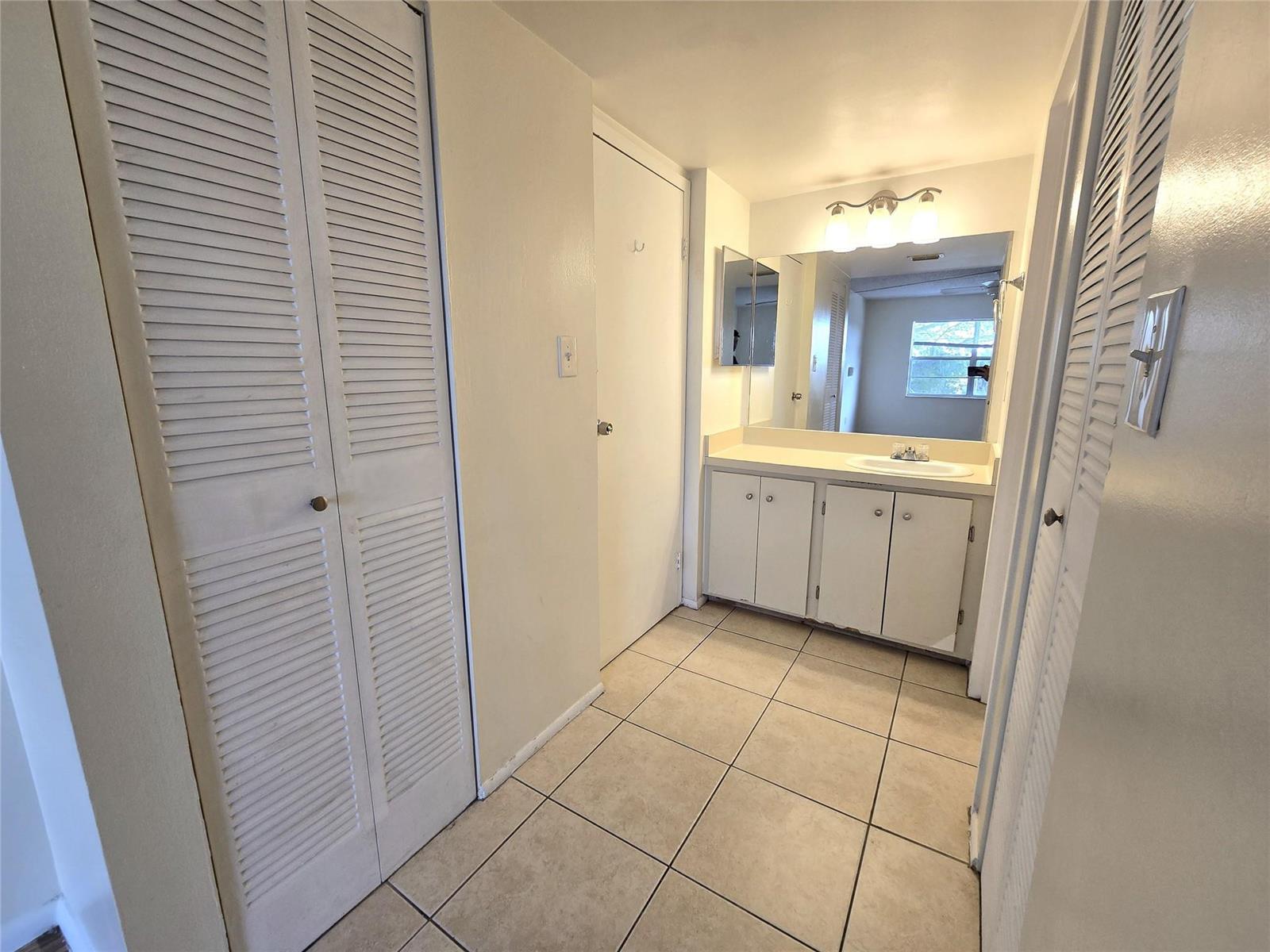 A bathroom features a vanity with a sink, tiled floors, and louvered closet doors — 4334 NW 9th Avenue # 3B, Deerfield Beach FL 33064, DEERFIELD BEACH, FL
