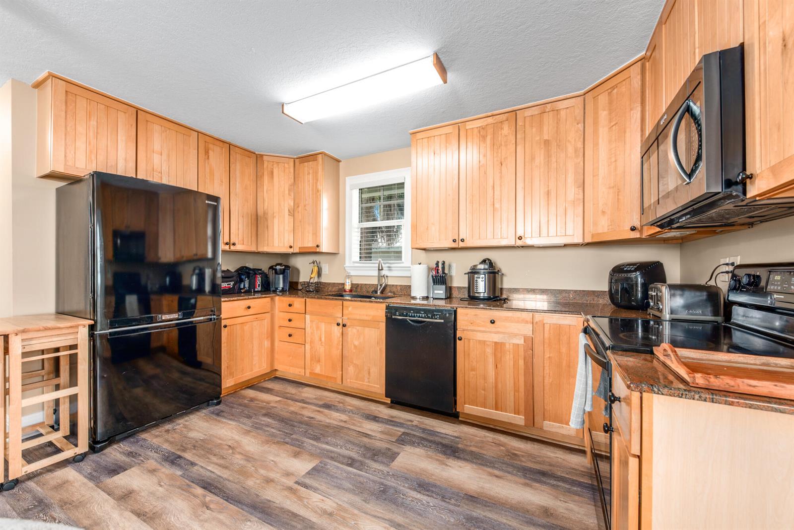 A kitchen features light wood cabinets, black appliances, dark countertops, and wood-look flooring — 404 SW Camden Avenue, Stuart FL 34994, STUART, FL
