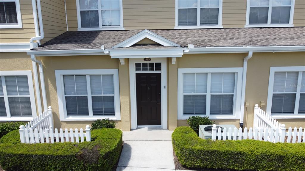An exterior view of a tan townhouse entrance with a dark door and white fencing — 2205 SAN VITTORINO CIRCLE UNIT 104, KISSIMMEE, FL
