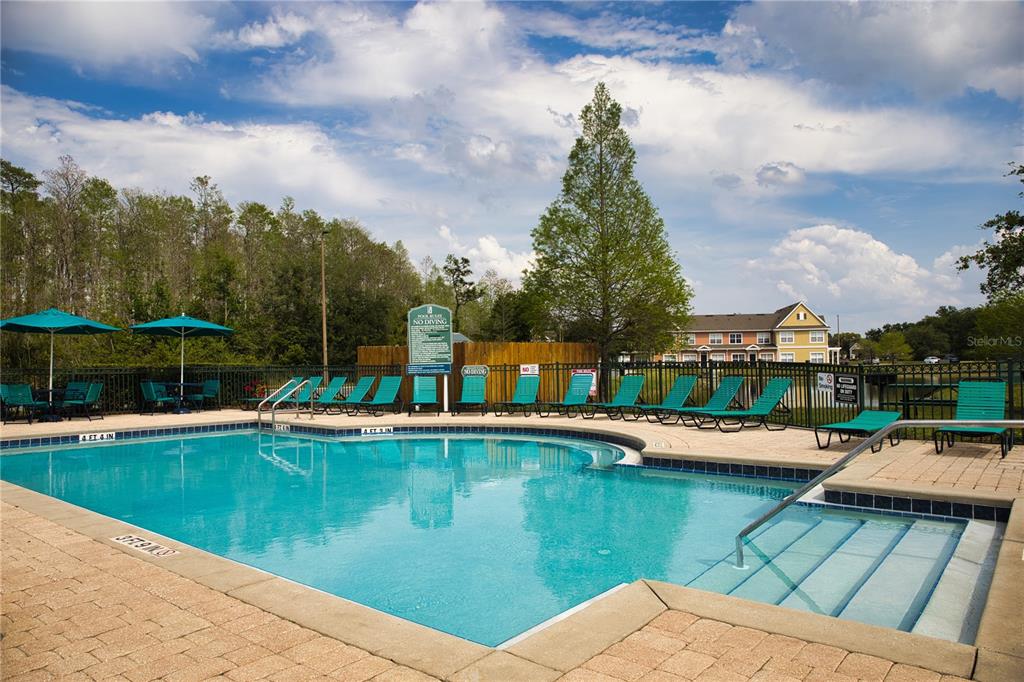 An outdoor swimming pool with lounge chairs and umbrellas sits in front of a building — 2205 SAN VITTORINO CIRCLE UNIT 104, KISSIMMEE, FL