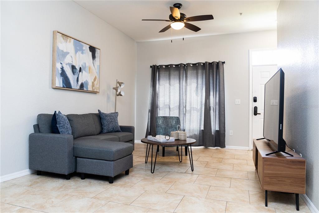 A living room features a gray sectional sofa, a round coffee table, and a television — 2205 SAN VITTORINO CIRCLE UNIT 104, KISSIMMEE, FL