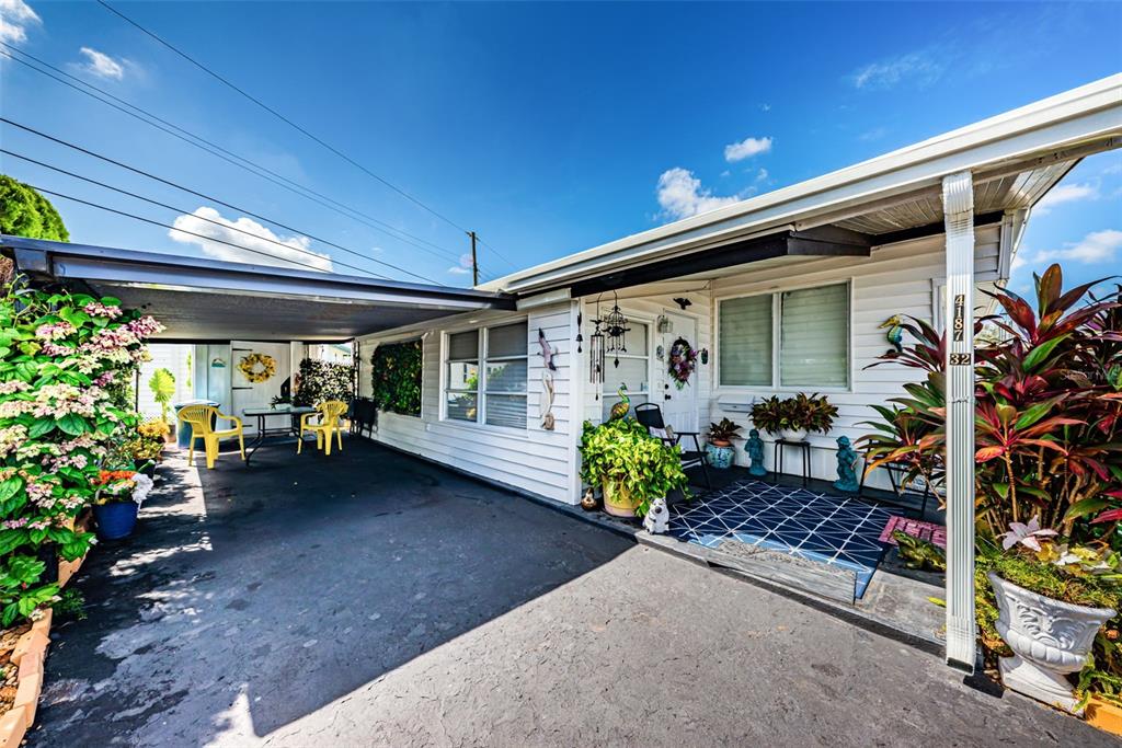 A white house exterior features a covered carport, a small front porch, and potted plants — 4187 72ND STREET N UNIT 32, ST PETERSBURG, FL