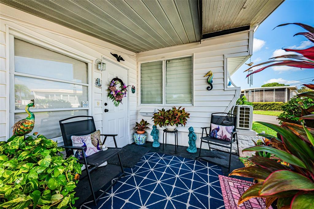 A covered porch features a blue patterned rug, two chairs, potted plants, and decor — 4187 72ND STREET N UNIT 32, ST PETERSBURG, FL