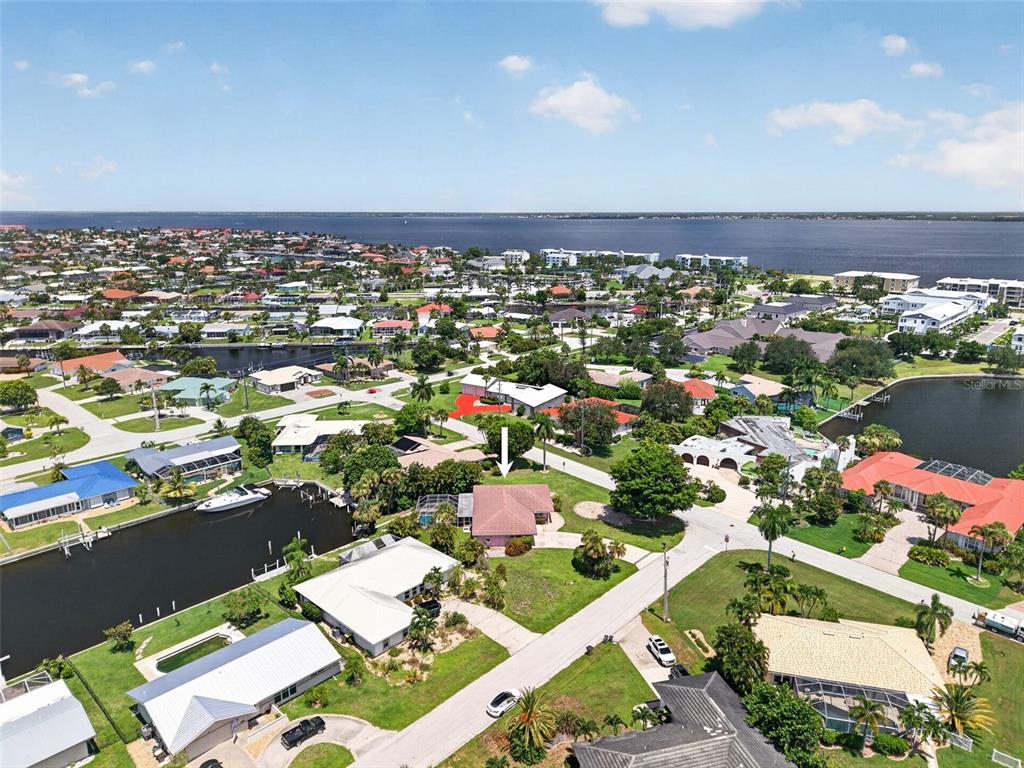 An aerial view shows a residential neighborhood with a pink house highlighted by a white arrow — 401 NORMA COURT, PUNTA GORDA, FL