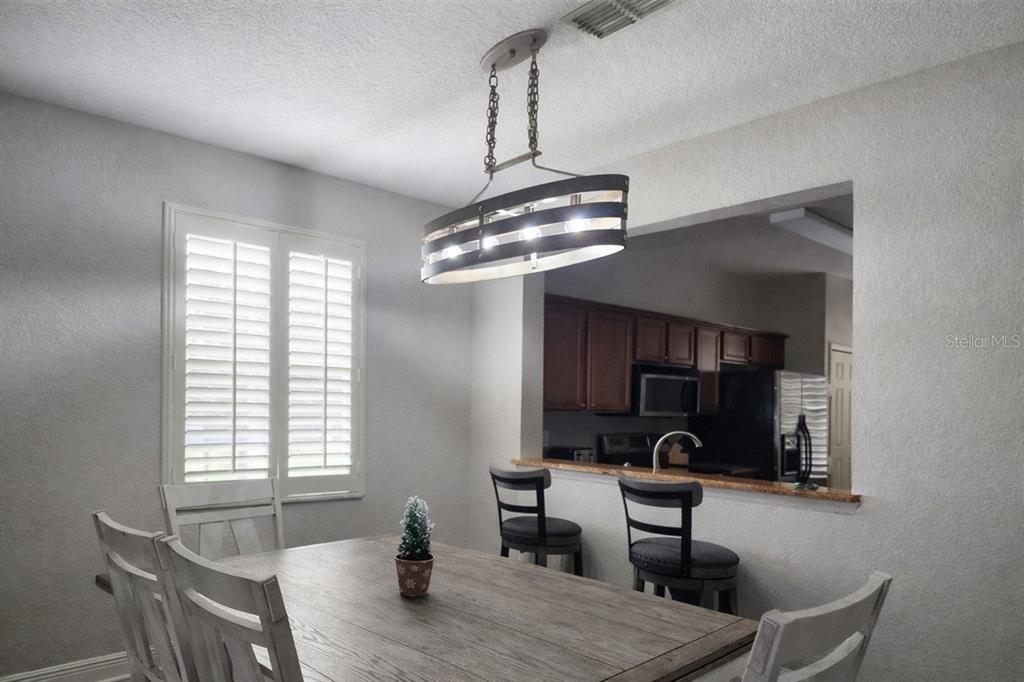 A dining area features a wooden table, a modern chandelier, and a breakfast bar opening — 3500 CALABRIA AVENUE, DAVENPORT, FL