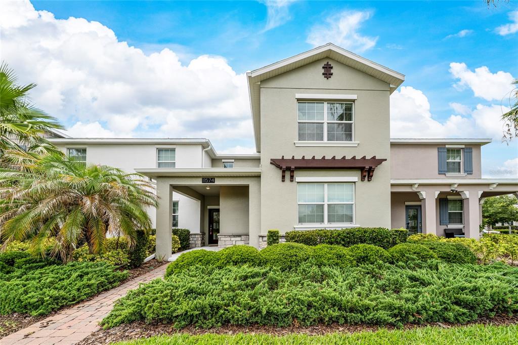 A two-story house with a beige stucco exterior, a covered entryway, and a landscaped front yard — 11574 COMIC ALLEY, ORLANDO, FL