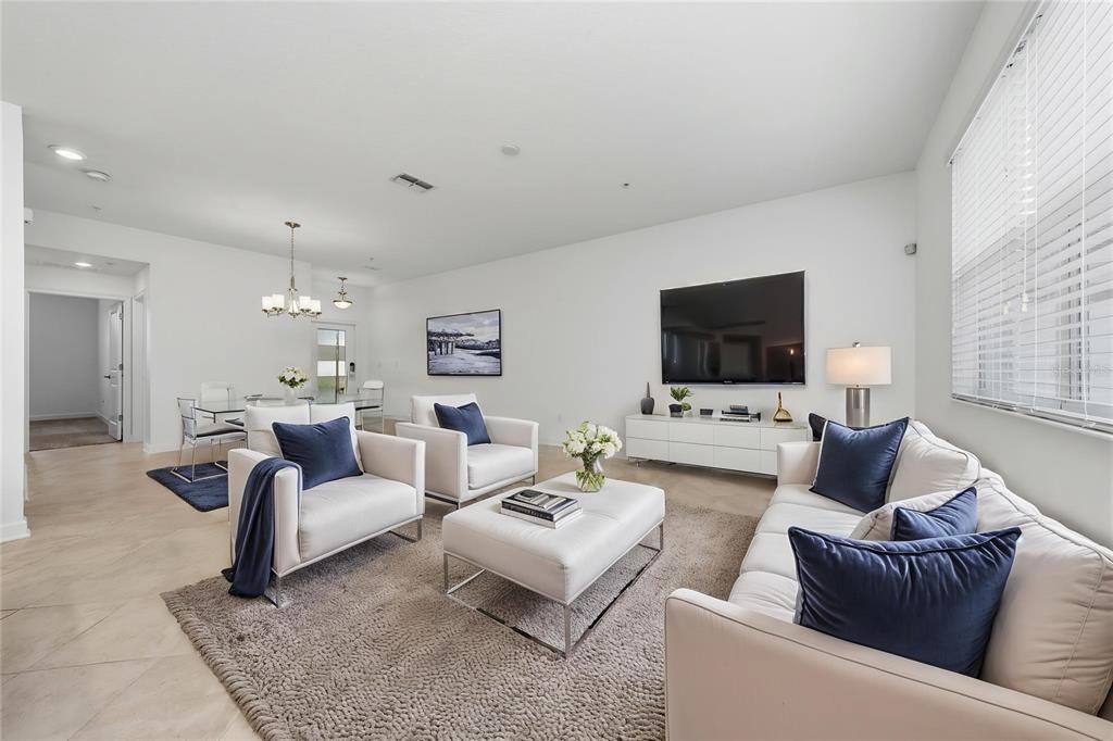A bright living room features white furniture, blue accent pillows, and a large wall-mounted television — 11574 COMIC ALLEY, ORLANDO, FL