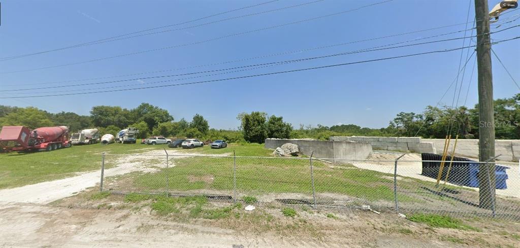 A fenced, partially paved outdoor lot contains construction equipment, several parked vehicles, and concrete barriers — APPALOOSA HILL ROAD, POLK CITY, FL