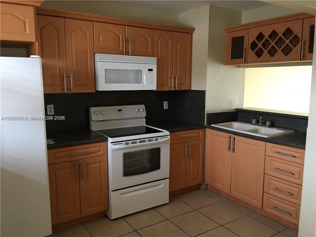 A kitchen features light wood cabinets, dark countertops, a white stove, and a white refrigerator — 315 NW 109th Ave # 207, Miami FL 33172, MIAMI, FL