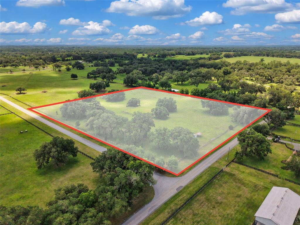 An aerial view shows a fenced, grassy plot of land bordered by a paved road — Lot 10 NW 123RD LANE, MORRISTON, FL