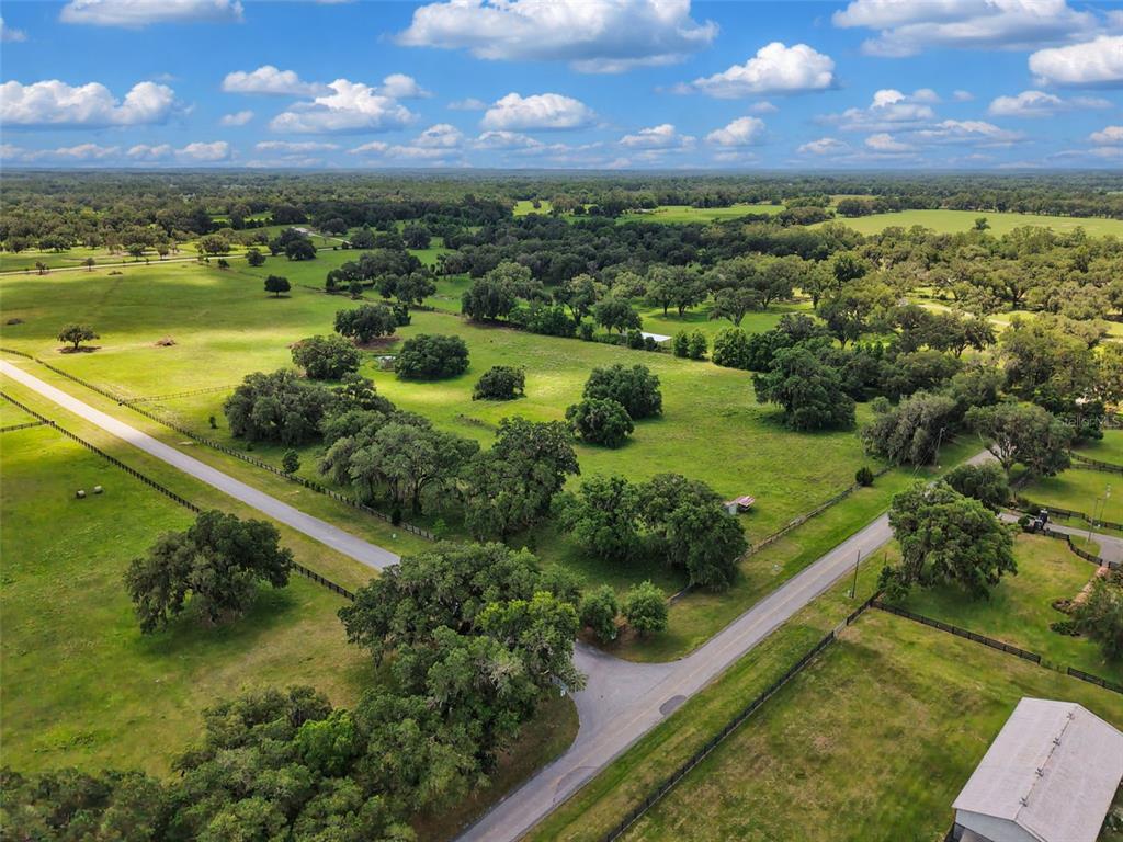 An aerial view shows a rural landscape with green pastures, scattered oak trees, and roads — Lot 10 NW 123RD LANE, MORRISTON, FL