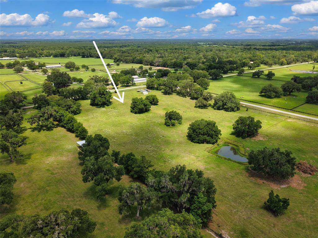 An aerial view shows a large, grassy pasture with scattered trees and a small pond — Lot 10 NW 123RD LANE, MORRISTON, FL