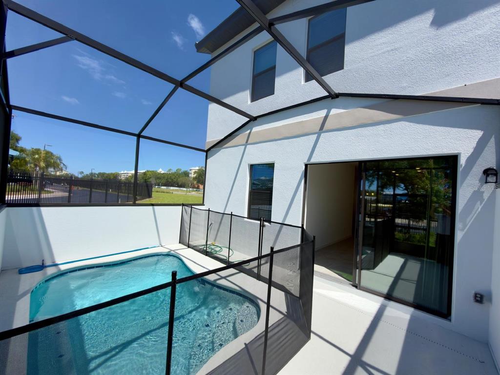 A small swimming pool with a safety fence sits inside a screened-in patio area — 10592 EBB TIDE LANE, ORLANDO, FL