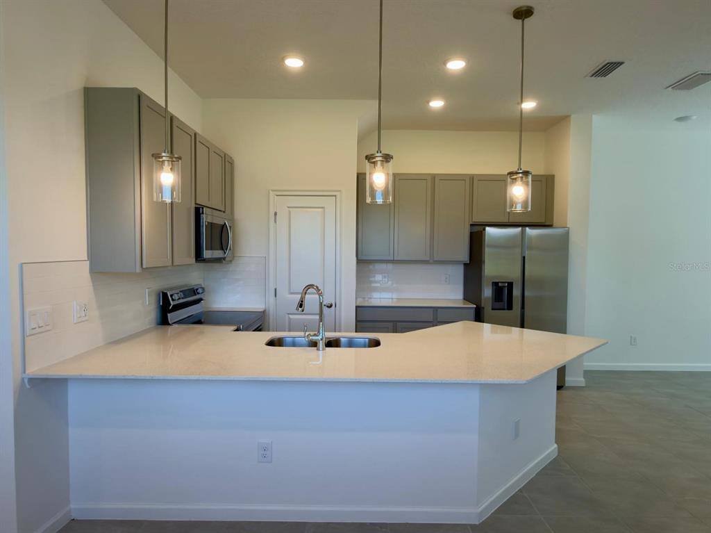 A kitchen features gray cabinets, stainless steel appliances, and a light-colored countertop island — 10592 EBB TIDE LANE, ORLANDO, FL