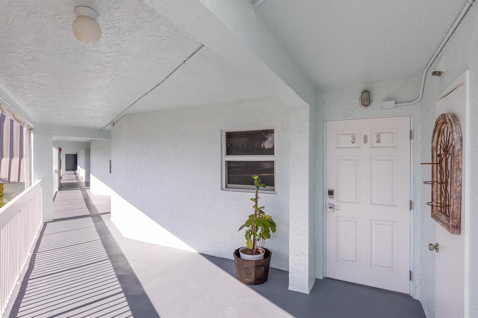 An exterior apartment hallway features a white door labeled 302, a potted plant, and railings — 961 S Ocean Drive # 302, Deerfield Beach FL 33441, DEERFIELD BEACH, FL
