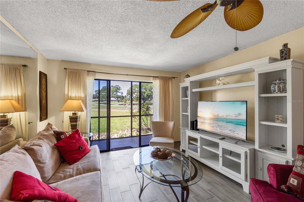 A living room features a white entertainment center, glass coffee table, and sliding glass doors — 4119 61ST AVENUE TERRACE W UNIT 102, BRADENTON, FL