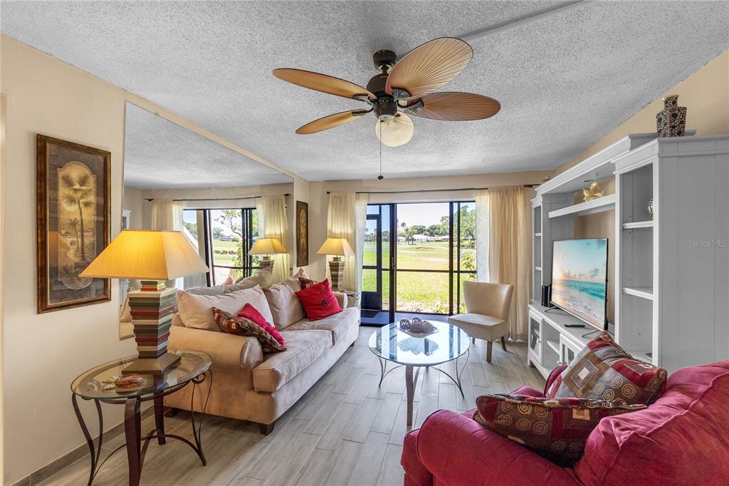 A living room features a beige sofa, red accent pillows, a glass coffee table, and tile flooring — 4119 61ST AVENUE TERRACE W UNIT 102, BRADENTON, FL