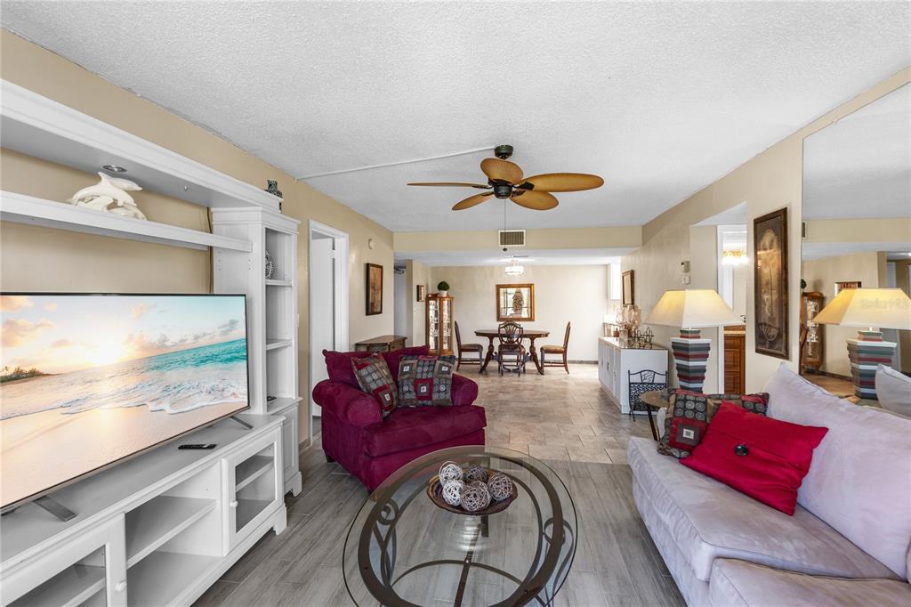 A living room with a television, a maroon armchair, a sofa, and a dining area — 4119 61ST AVENUE TERRACE W UNIT 102, BRADENTON, FL