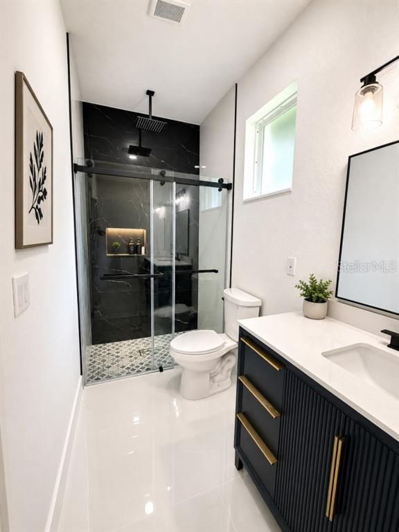 A modern bathroom features a black-tiled walk-in shower, a white toilet, and a navy vanity — 3476 SE HWY 484, BELLEVIEW, FL
