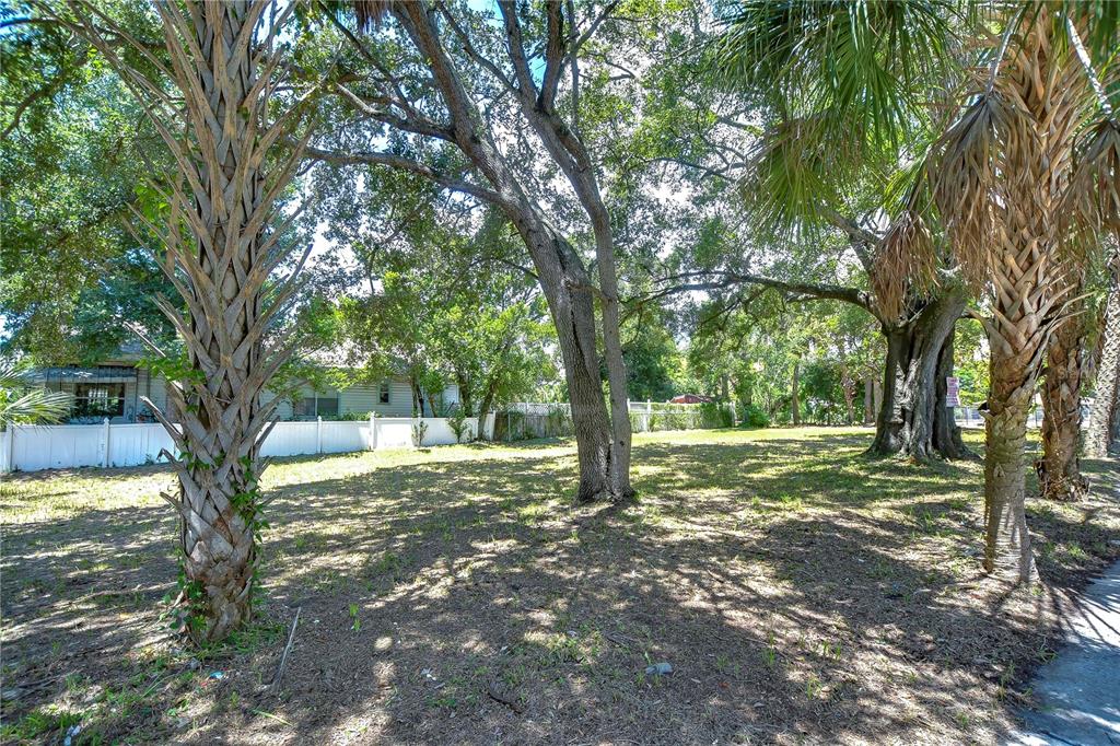A grassy, tree-shaded vacant lot is enclosed by a white vinyl fence — 1522 E 26TH AVENUE, TAMPA, FL
