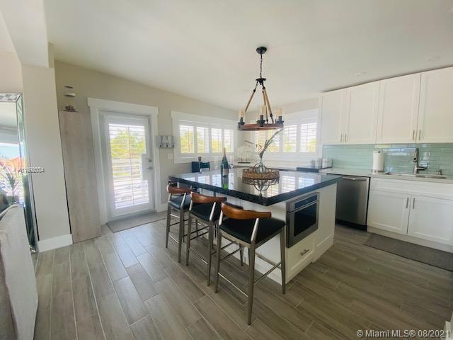 A kitchen features a granite-topped island with three bar stools and white cabinetry — 203 Atlantic Blvd # 203, Key Largo FL 33037, KEY LARGO, FL