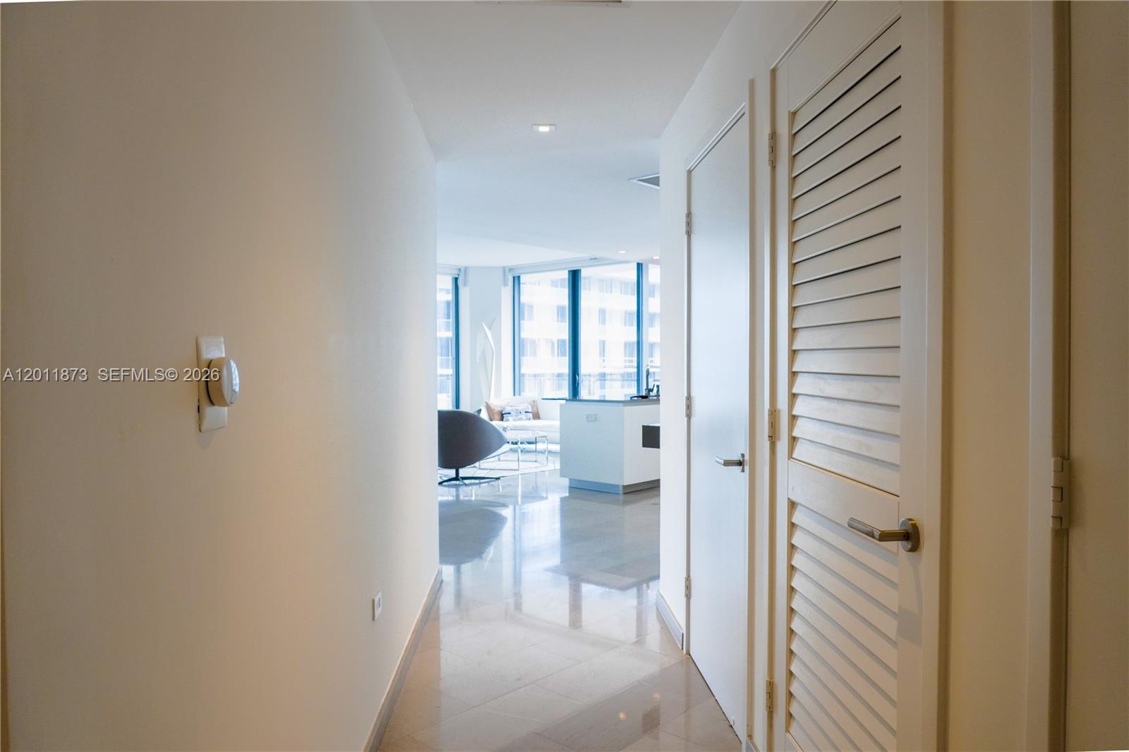 A hallway with light tile flooring leads toward a bright living area with floor-to-ceiling windows — 88 SW 7 # 2112, Miami FL 33130, MIAMI, FL