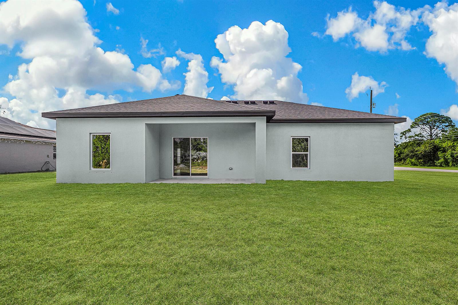 The exterior of a single-story house features a light gray stucco finish and a backyard — 7945 105th Court, Vero Beach FL 32967, VERO BEACH, FL
