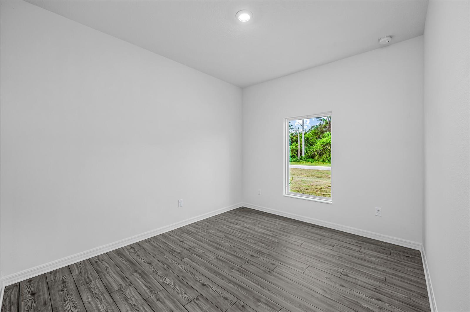 An empty room with white walls, grey wood-look flooring, and a single window — 7945 105th Court, Vero Beach FL 32967, VERO BEACH, FL