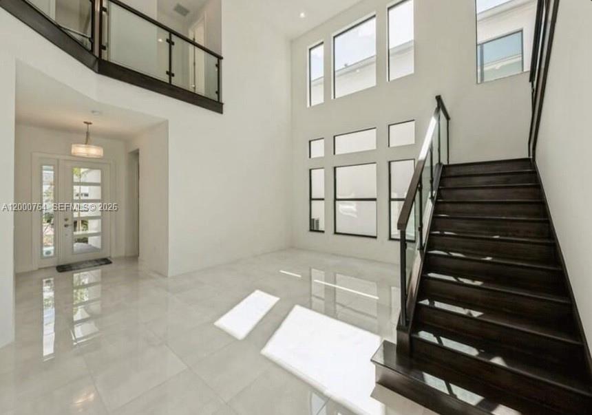 A bright, high-ceilinged foyer features white tile floors, a dark wood staircase, and glass railings — 17041 Teton River Rd, Boca Raton FL 33496, BOCA RATON, FL