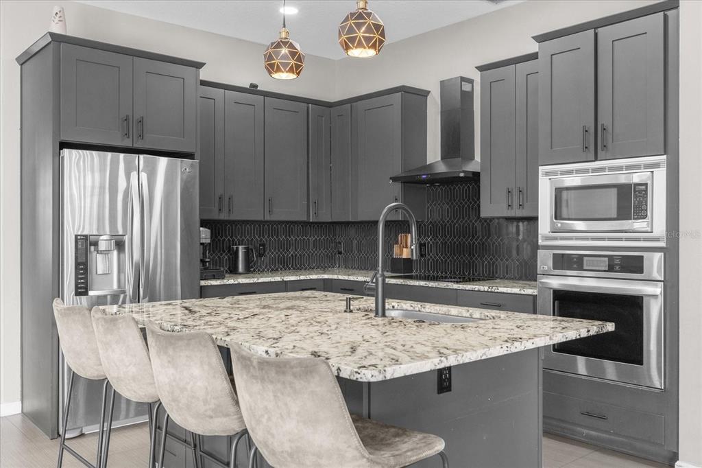 A modern kitchen features dark gray cabinetry, a granite island with bar seating, and stainless appliances — 10175 COVE LAKE DRIVE, ORLANDO, FL