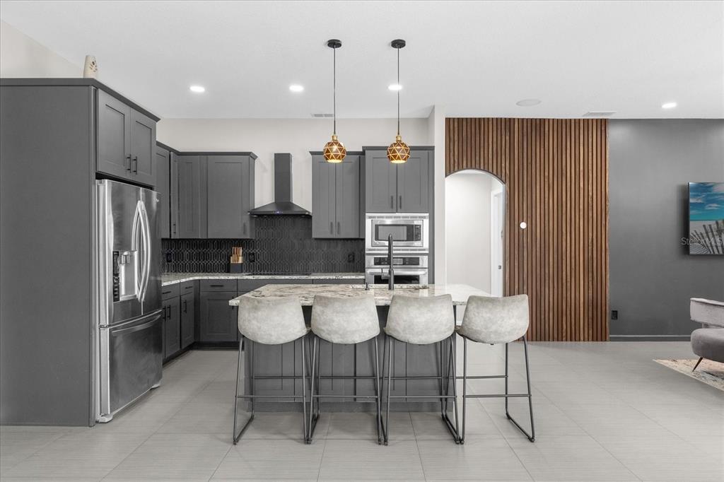 A modern kitchen features dark gray cabinetry, a marble-topped island, and a wood-slatted accent wall — 10175 COVE LAKE DRIVE, ORLANDO, FL