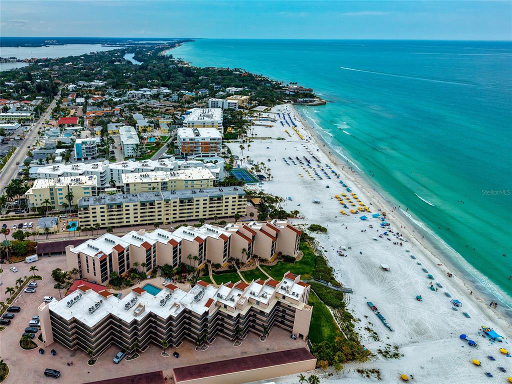 An aerial view shows beachfront condominiums, a white sand beach, and the turquoise ocean — 6480 MIDNIGHT PASS ROAD UNIT 503, SARASOTA, FL