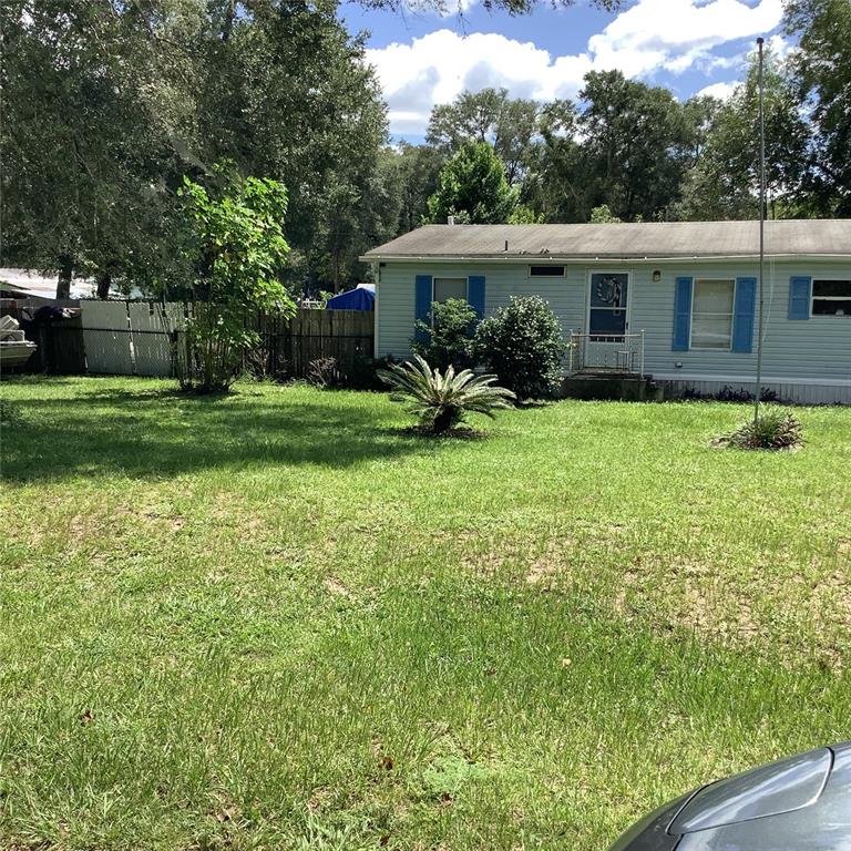 A light blue single-story house sits behind a large grassy yard with mature trees — 20406 BLUE WING ROAD, ALTOONA, FL