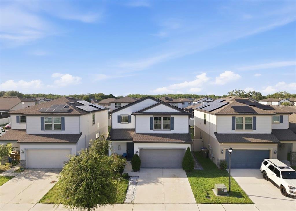 An exterior view of three two-story suburban houses with solar panels on their roofs — 3557 ROCK CREEK LANE, KISSIMMEE, FL