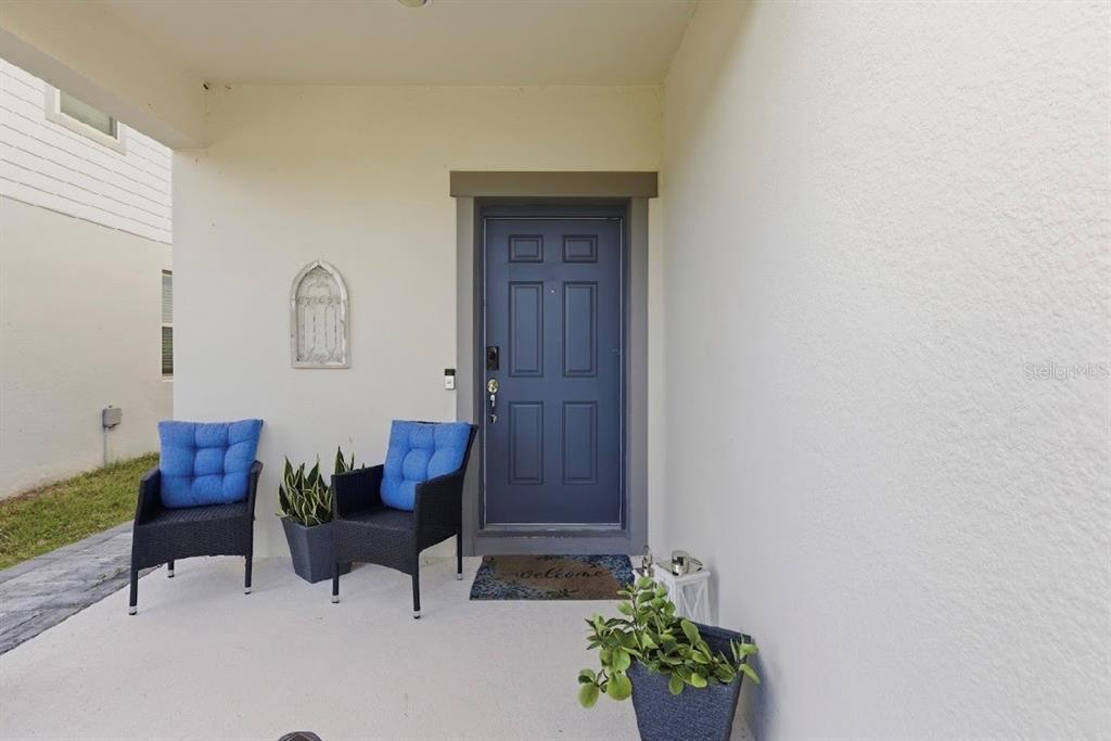 A covered front porch features a blue door, two chairs with blue cushions, and potted plants — 3557 ROCK CREEK LANE, KISSIMMEE, FL